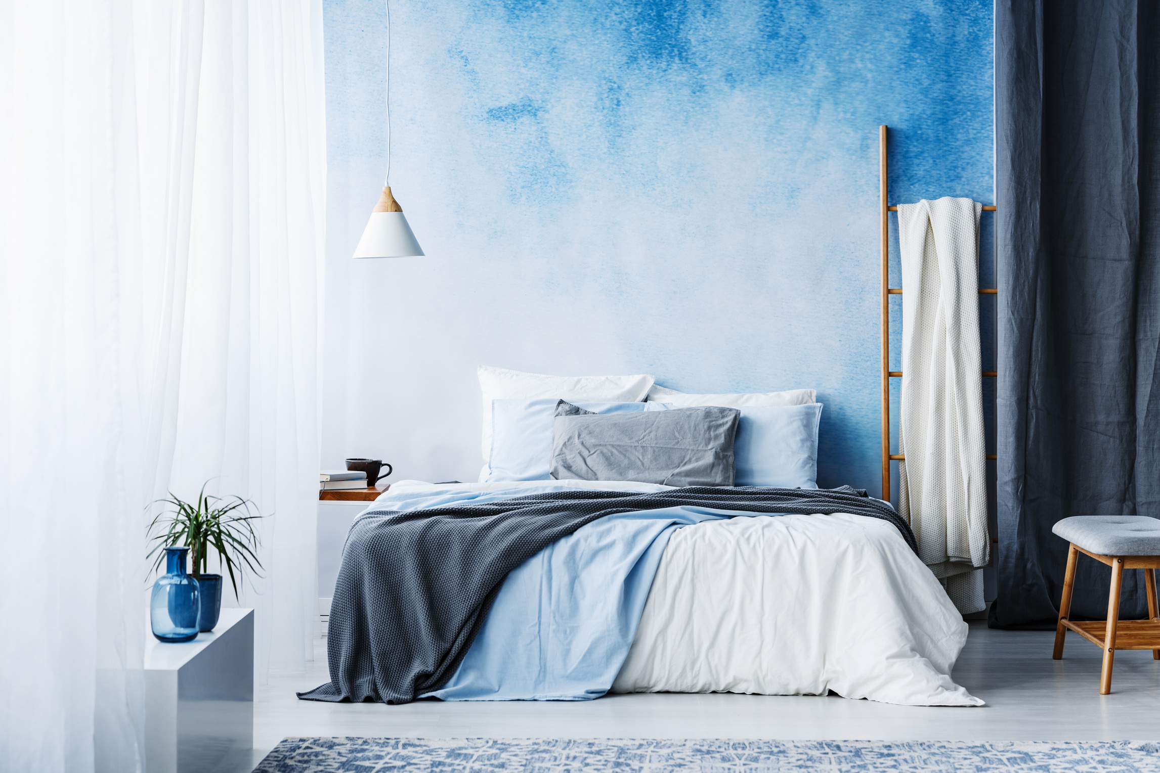 Grey and blue bedding on bed in spacious bedroom interior with ladder and plant